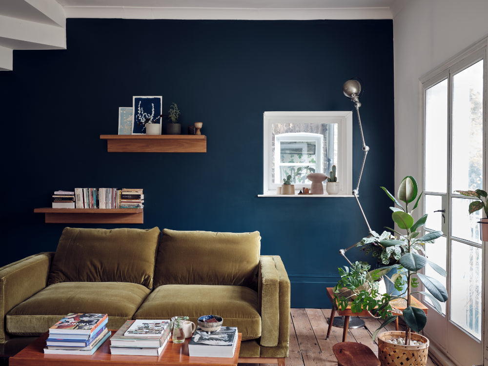 Modern living room with a green sofa, wooden coffee table, and dark blue wall.