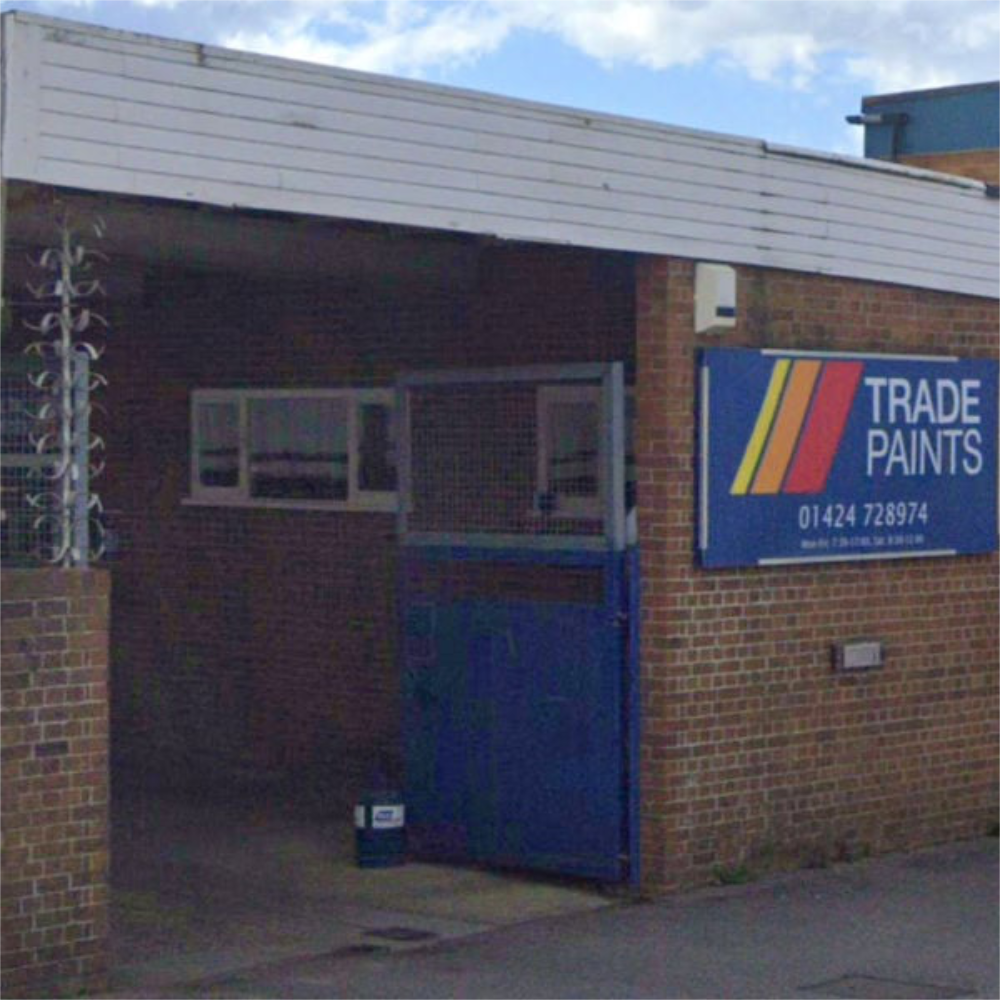 Brick building with a blue door and Trade Paints sign on a clear day